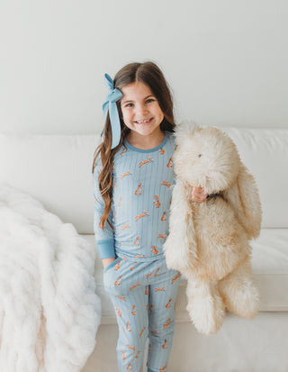 Young girl in blue pajamas holding a fluffy white bunny toy on a white couch.