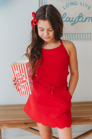 Young girl in a red dress holding popcorn with blue balloons and 'Long Live Playtime' sign in the background.