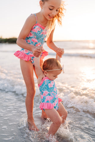 Two young girls in matching swimsuits playing in the water at the beach.