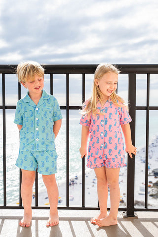 Two children, a boy and a girl, standing on a balcony with a waterfront view.