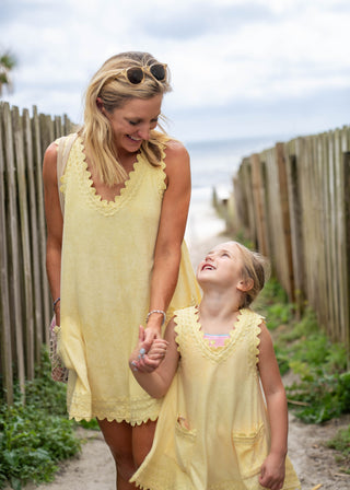 Woman and child in matching yellow dresses standing outdoors near a wooden fence.