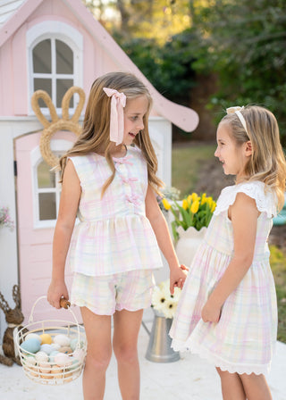 Two young girls in matching pastel outfits standing in front of a pink playhouse with Easter decorations.