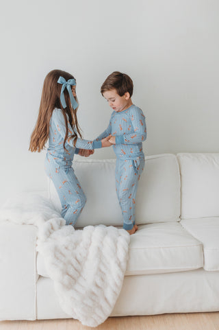 Two children in matching pajamas standing on a white couch with a white blanket.