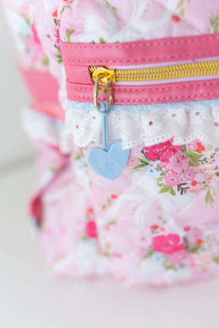 Floral-patterned pouch with pink zipper and heart-shaped tag on a light background