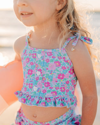 Child in a floral swimsuit standing on a beach with a blurred background