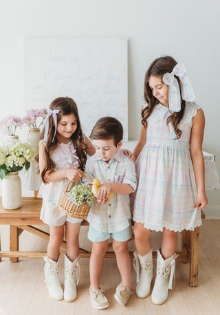 Three children in matching outfits standing in a room with a white wall and wooden floor.