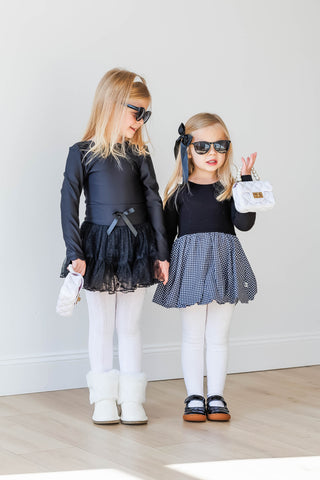 Two young girls in matching outfits with black tops and skirts, standing indoors.