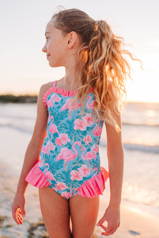 Young girl in a colorful swimsuit with floral and flamingo pattern on a beach.