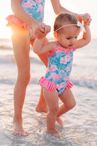 Two children in matching swimsuits standing in shallow water at the beach.