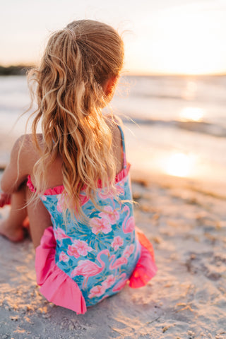 Child in a floral swimsuit sitting on a beach at sunset