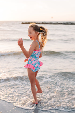 Young girl in a colorful swimsuit playing on a beach.