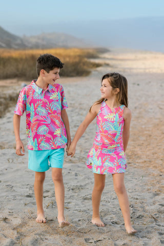 Two children in colorful beach outfits standing on a sandy beach with a clear sky.